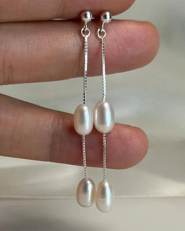 Pearl earrings held between fingers against a neutral background