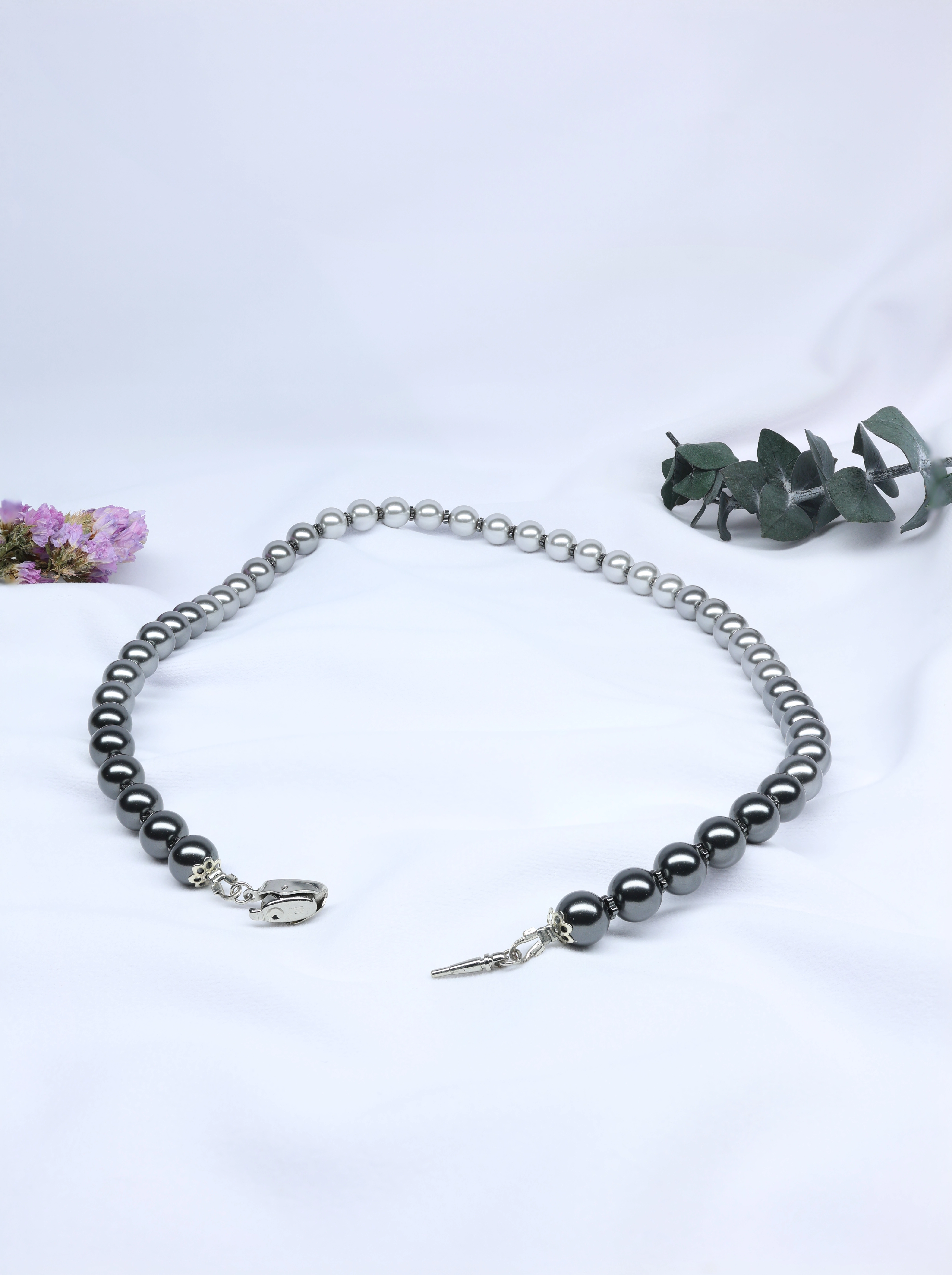 Pearl necklace on a white background with green leaves and flowers.