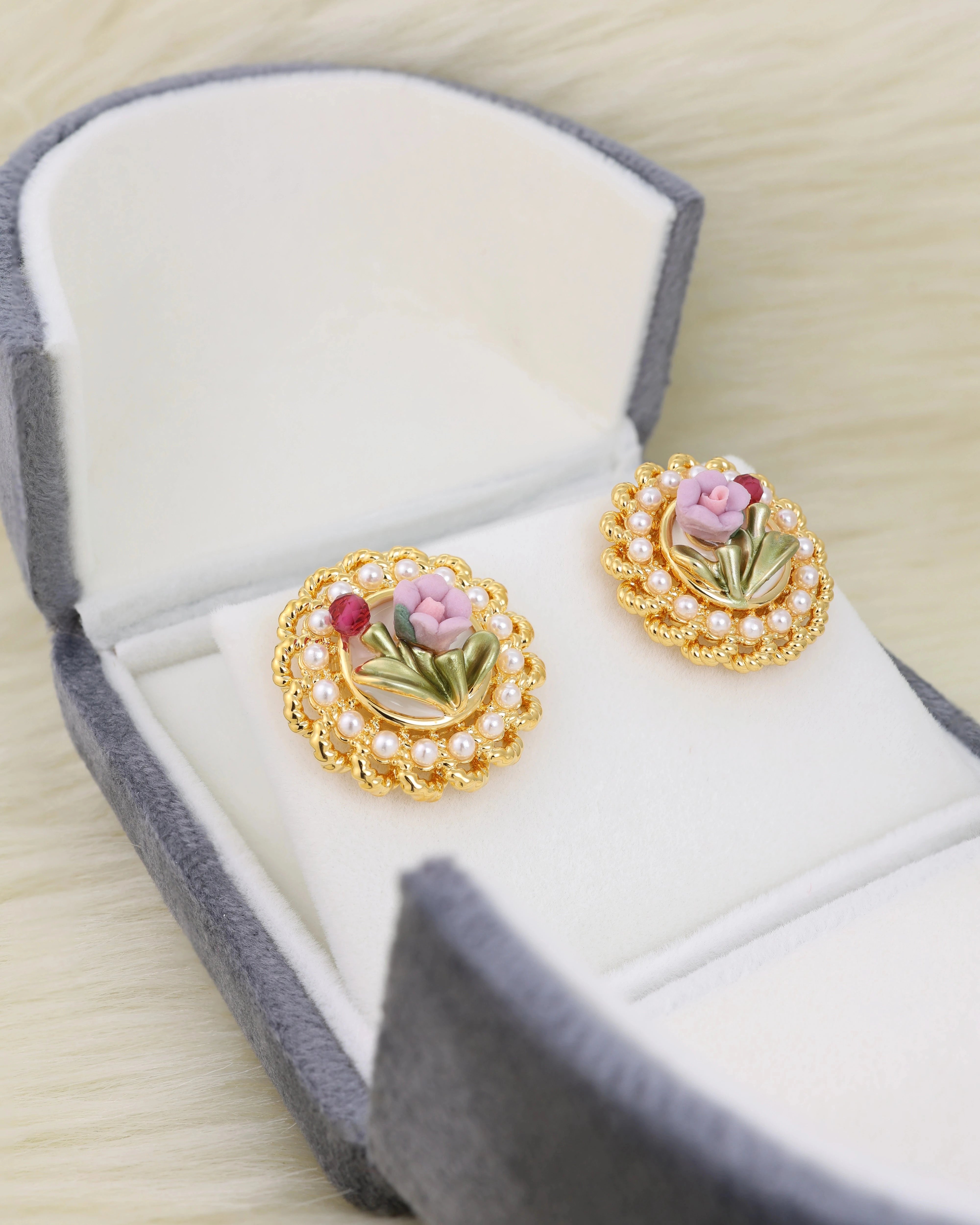 Gold earrings with floral design in a jewelry box on white fur