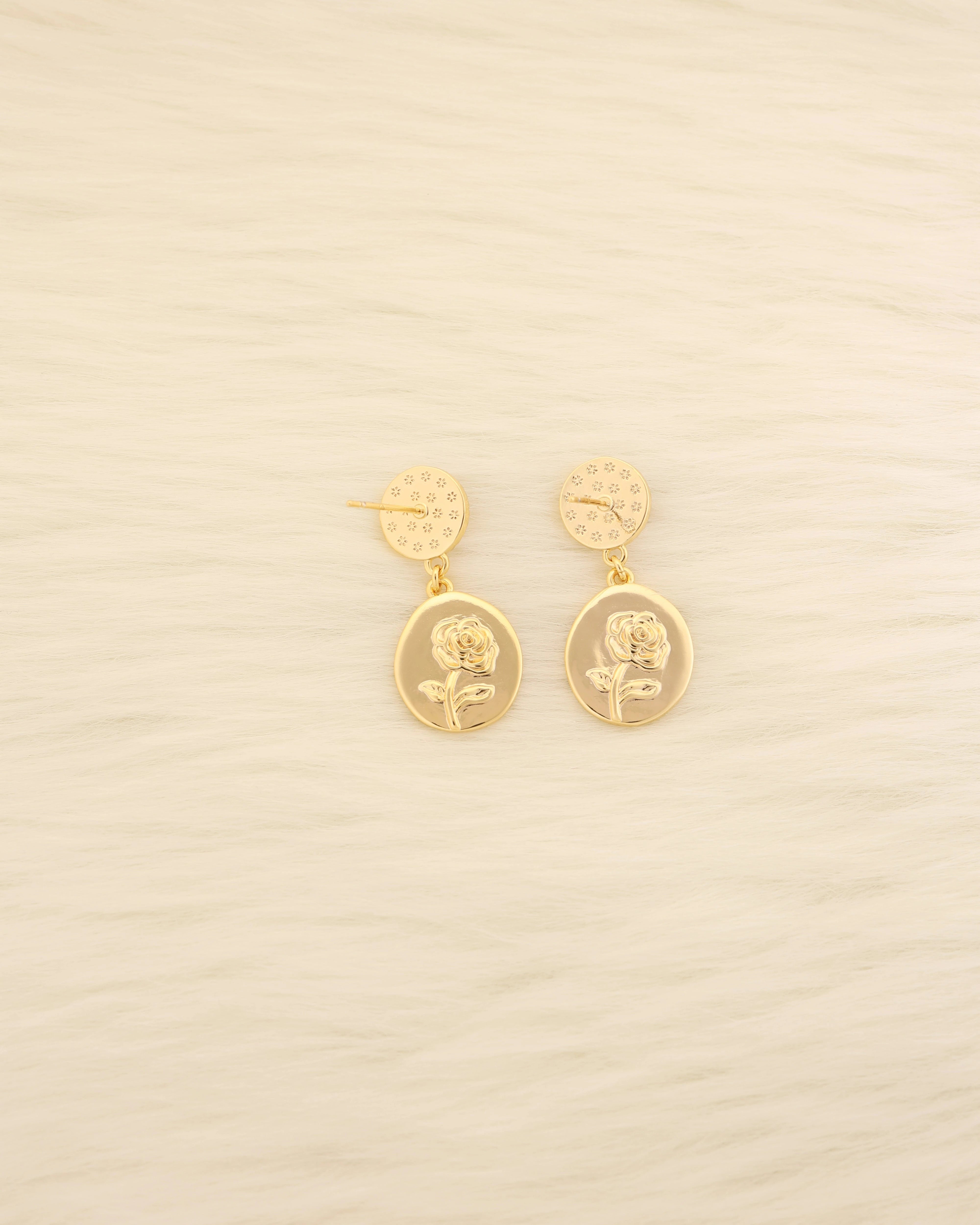 Gold earrings with floral designs on a beige background