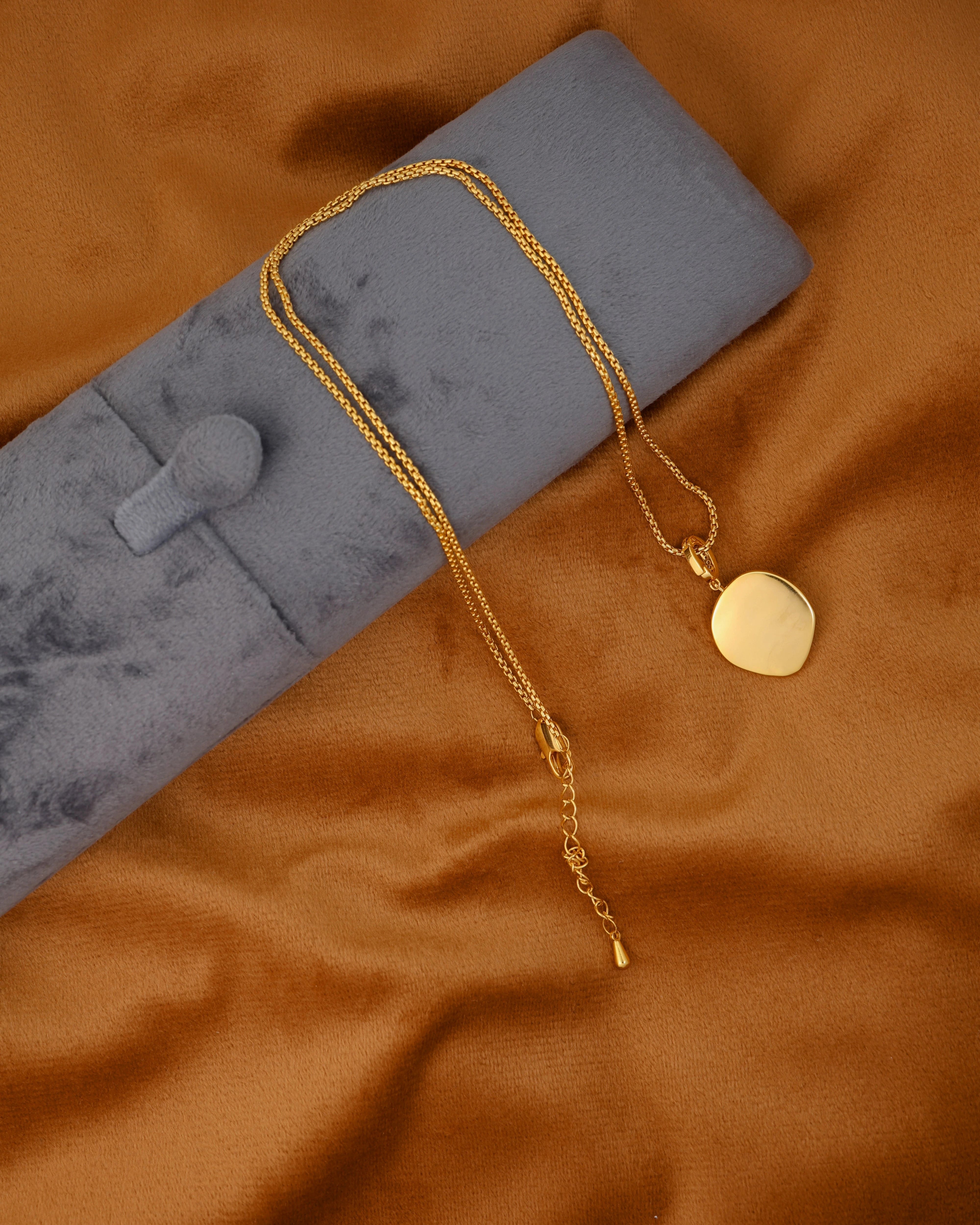 Gold necklace with a heart-shaped pendant on a brown fabric background