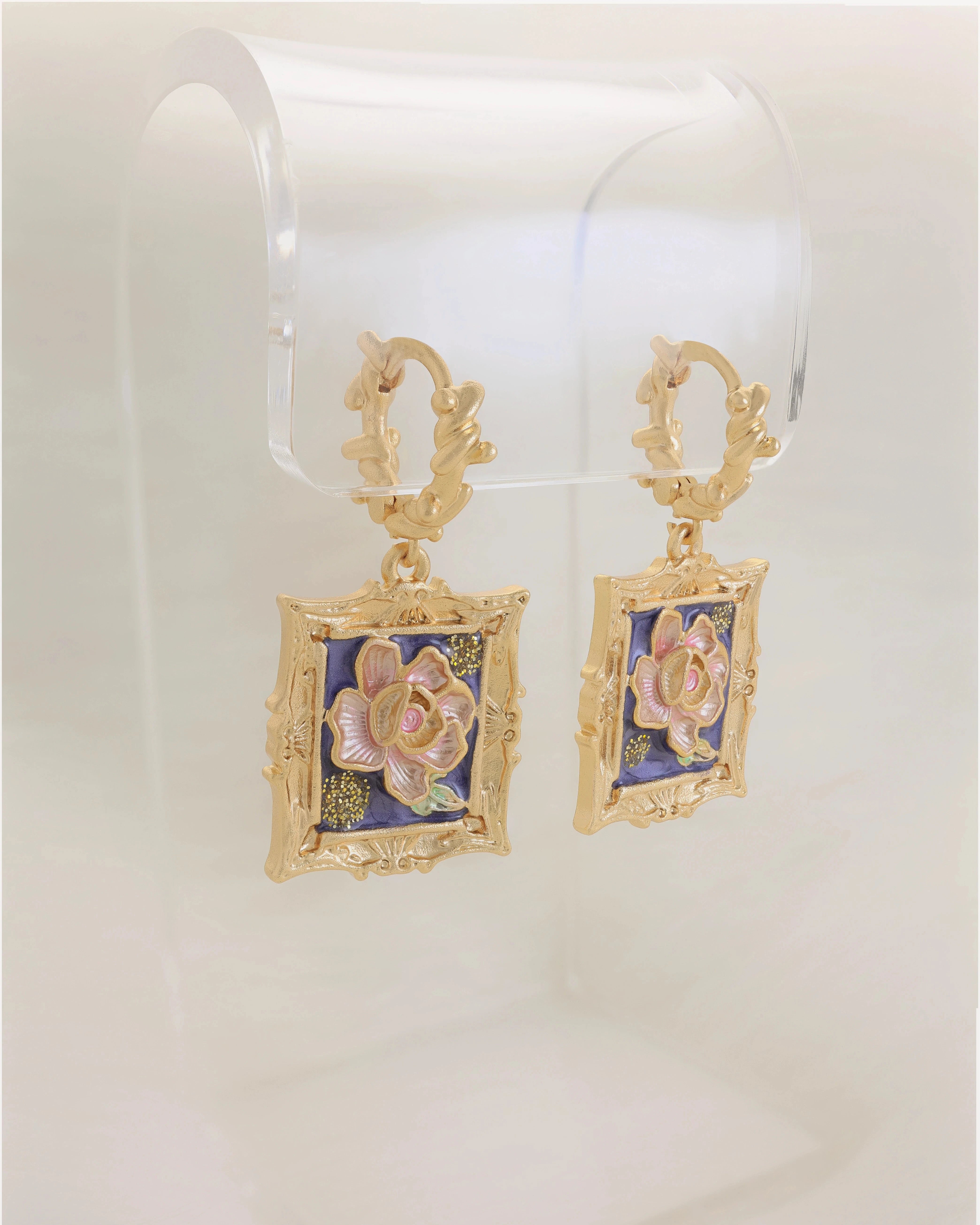 Gold earrings with floral design on a clear stand