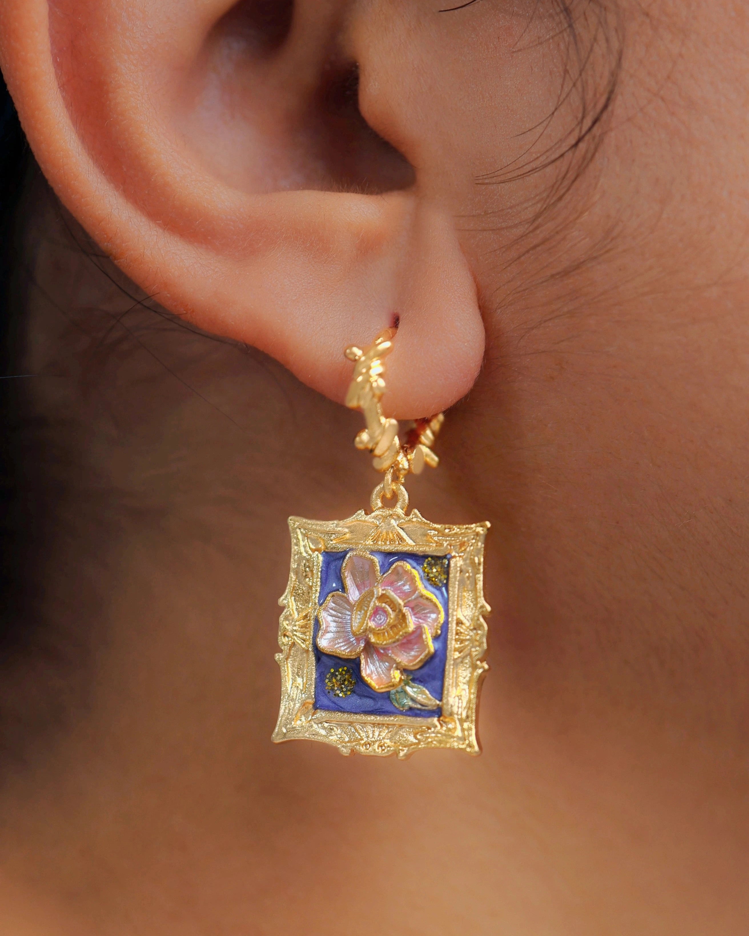 Gold earring with floral design worn on an ear