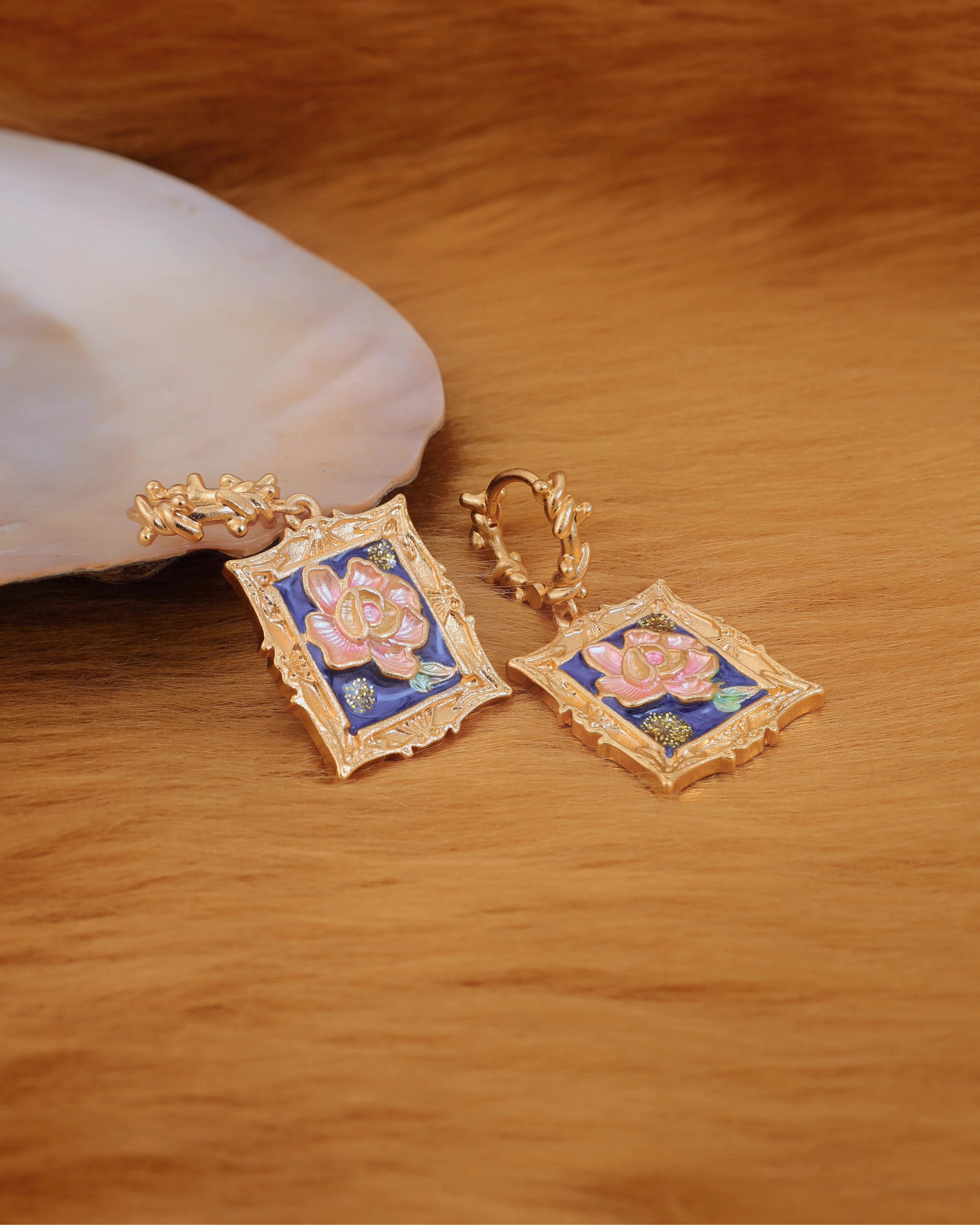 Gold earrings with floral design on a wooden surface