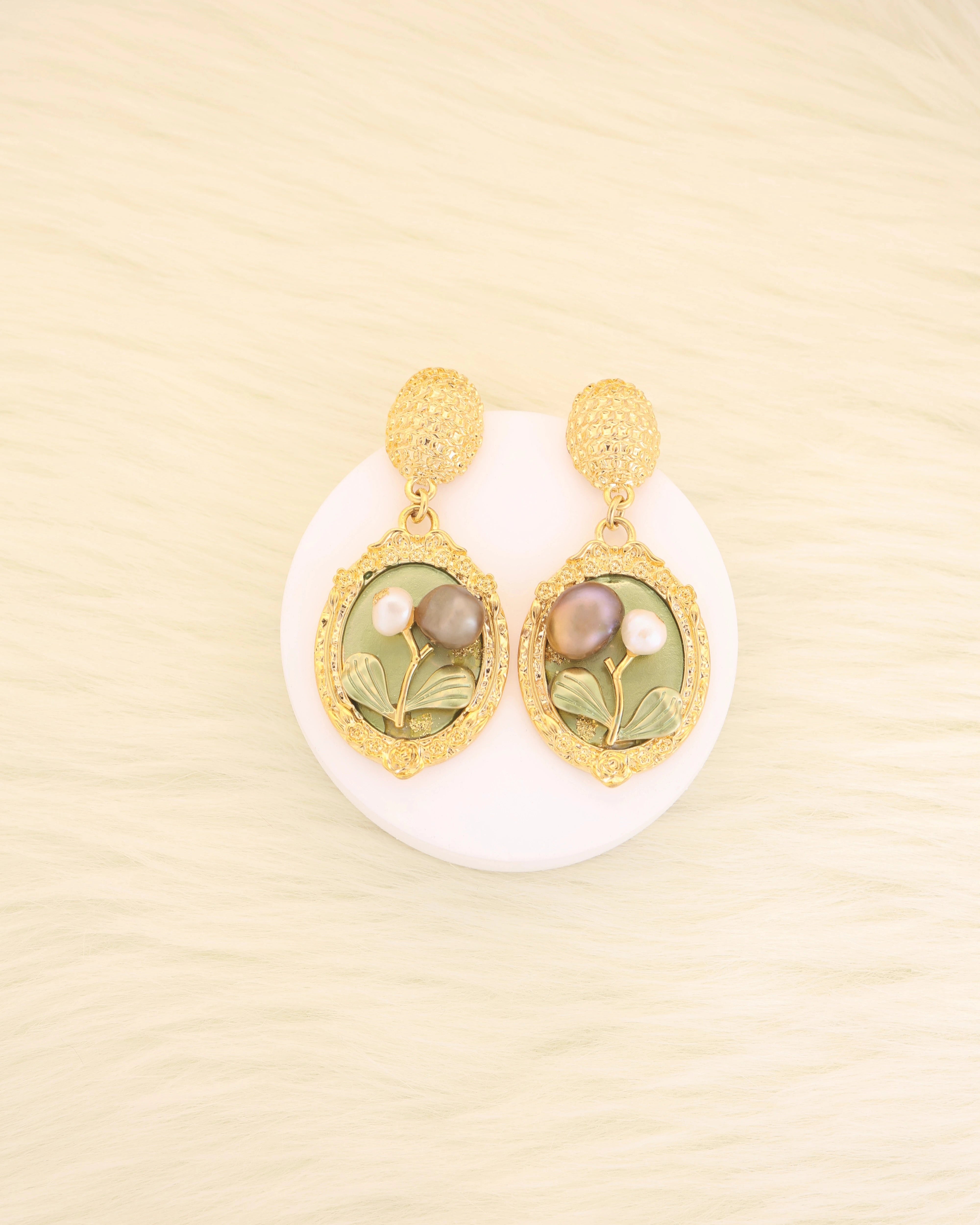 Pair of pearl gold platted earrings with green gemstones on a beige background