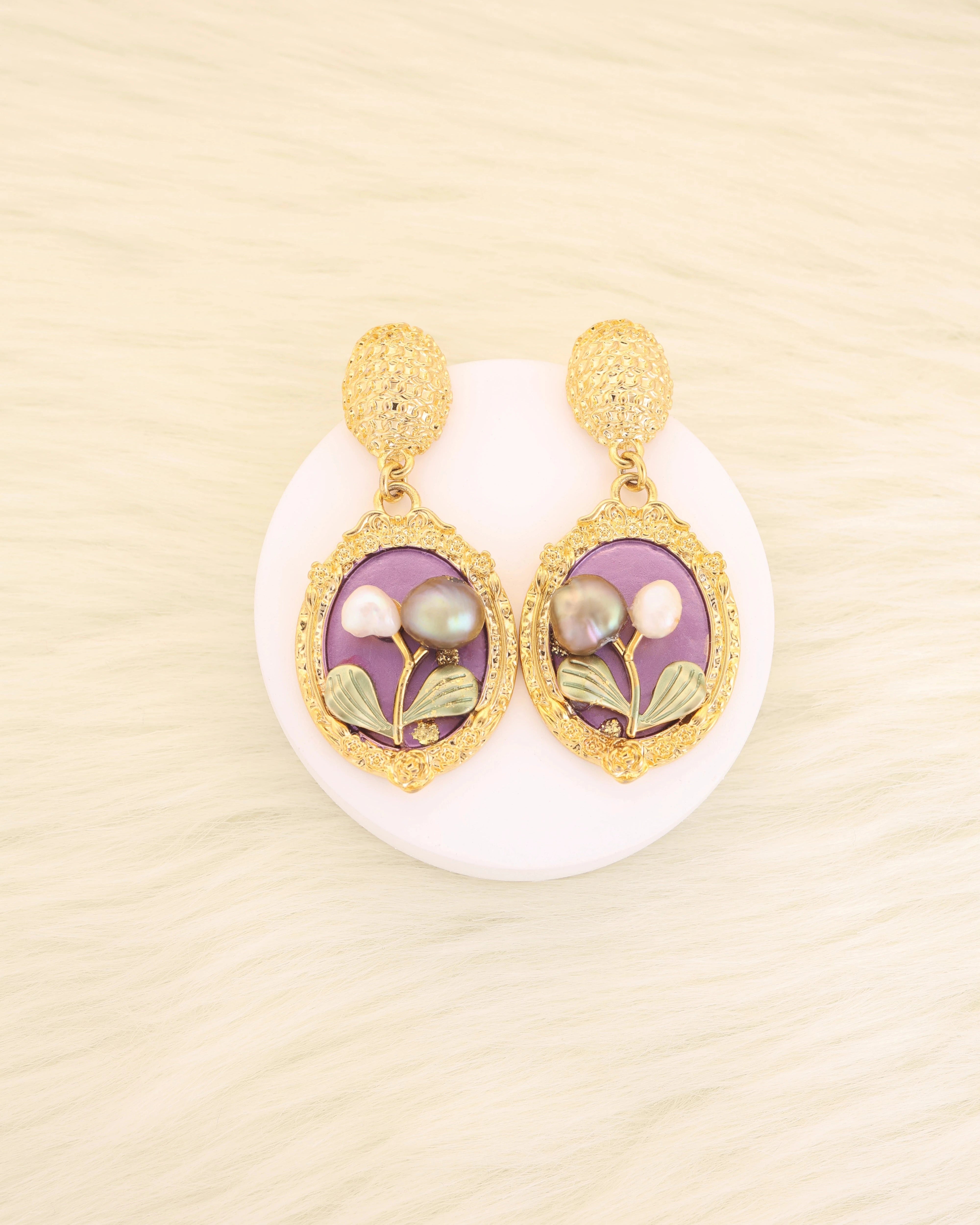 Pair of Pearl gold platted earrings with purple and green accents on a beige background