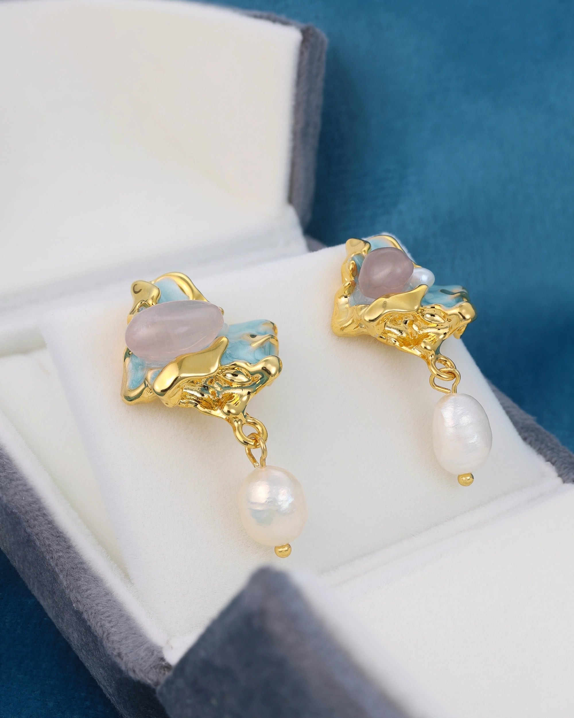 Gold earrings with gemstones and pearls on a white cushion