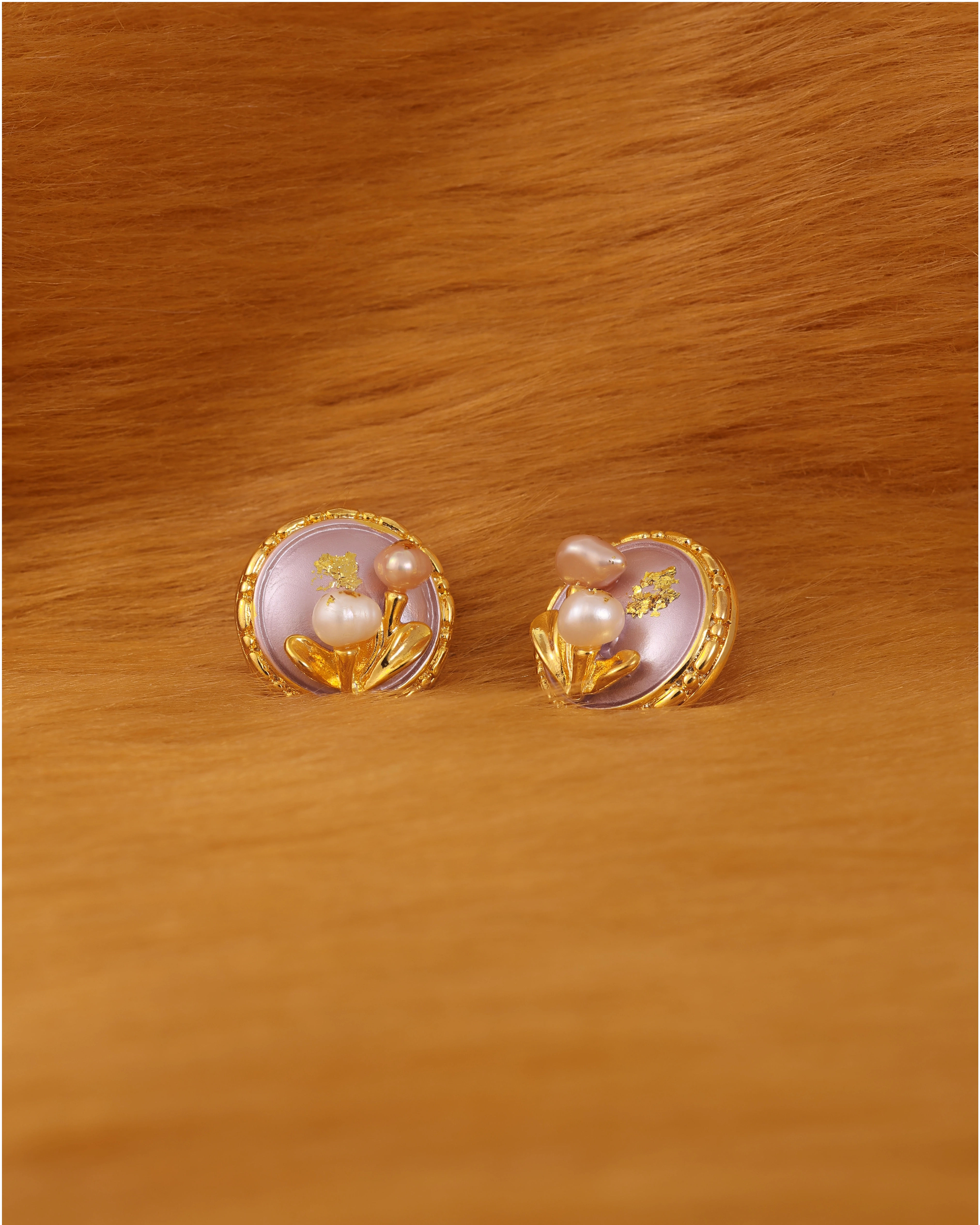 Gold earrings with pearl design on fur background
