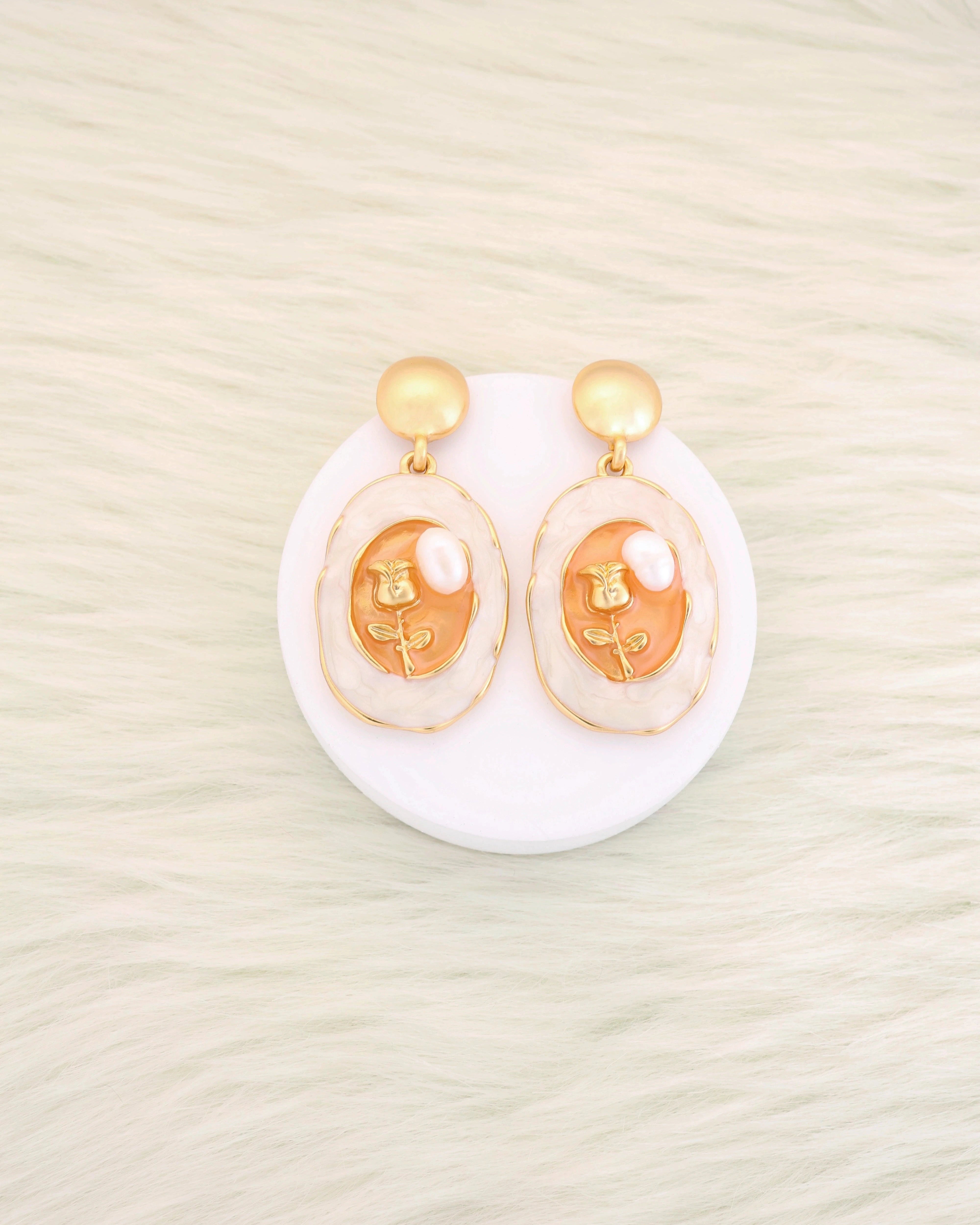Pair of earrings on a white circular stand against a textured beige background