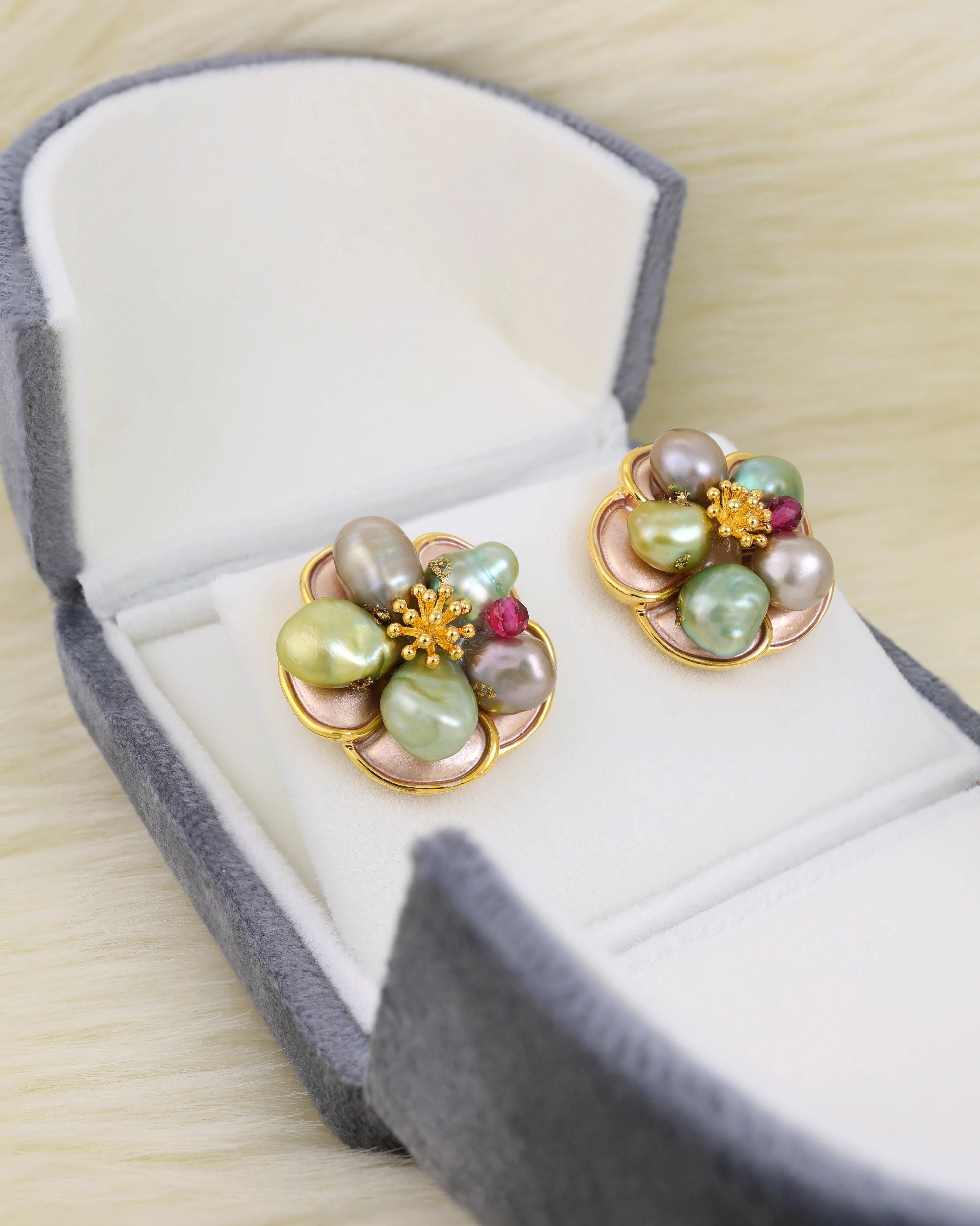 Pair of floral earrings with pearls and gemstones in a gray jewelry box.