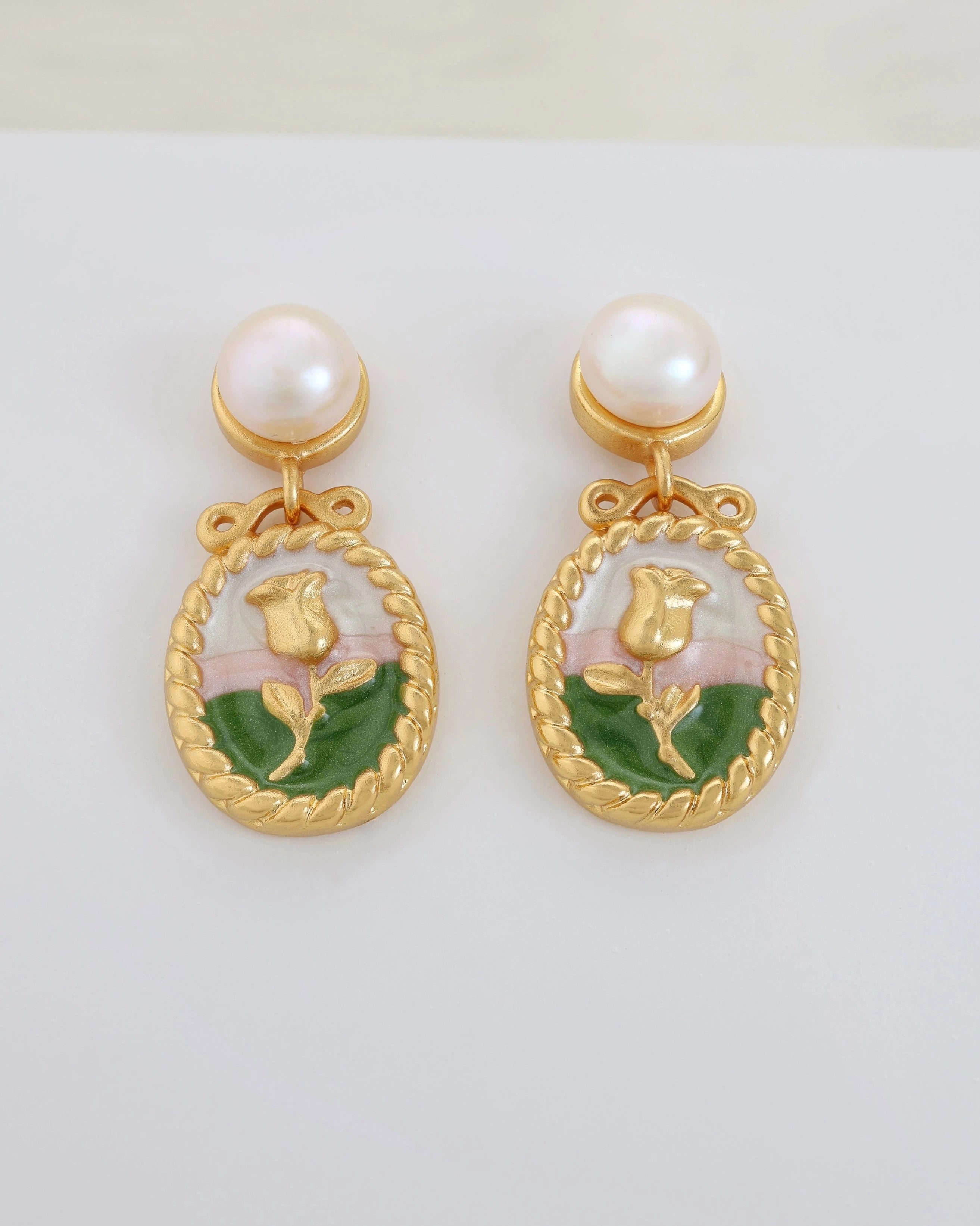 Pair of gold earrings with pearl tops and rose designs on a white background