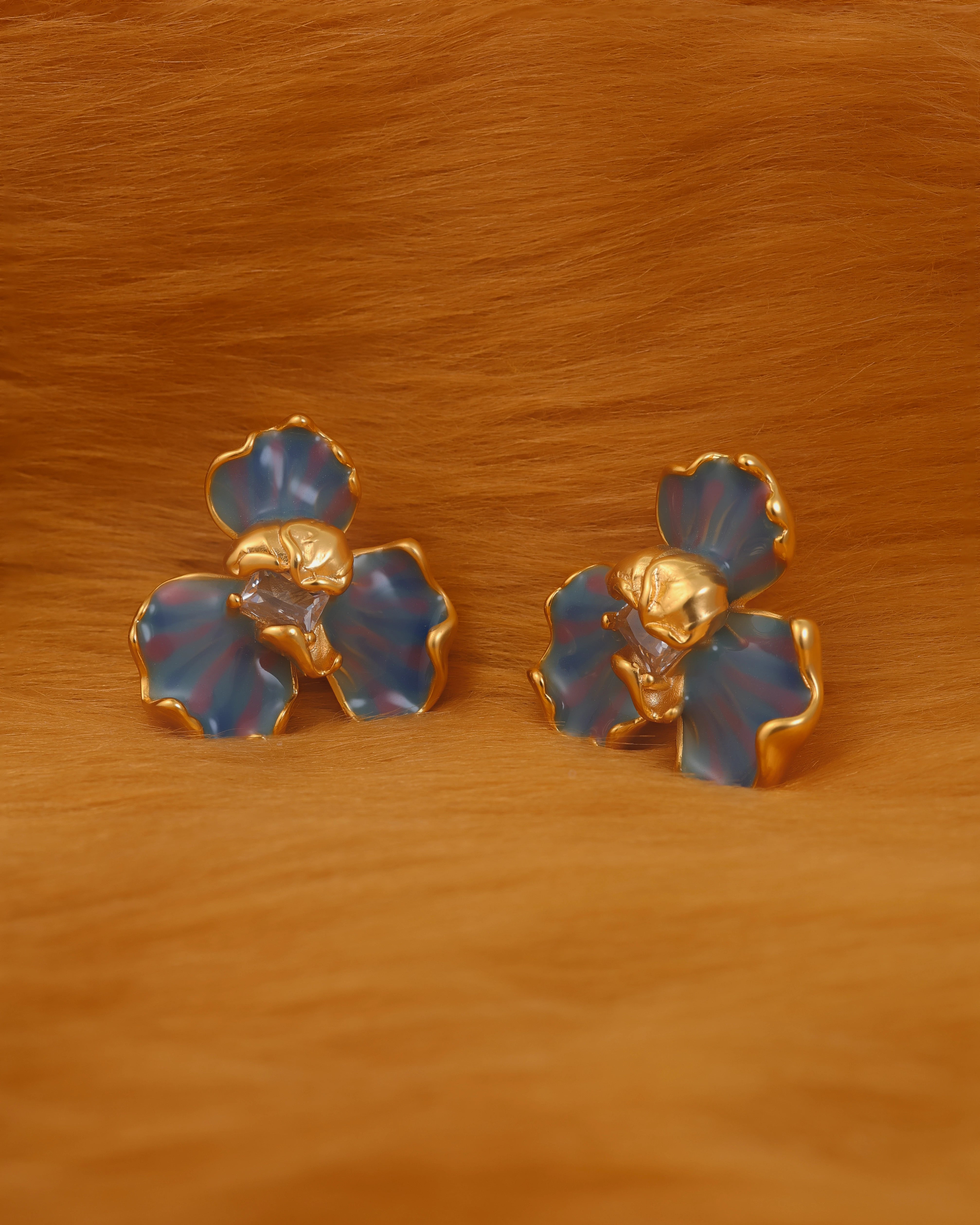 Pair of gold and blue flower-shaped earrings on a wooden surface