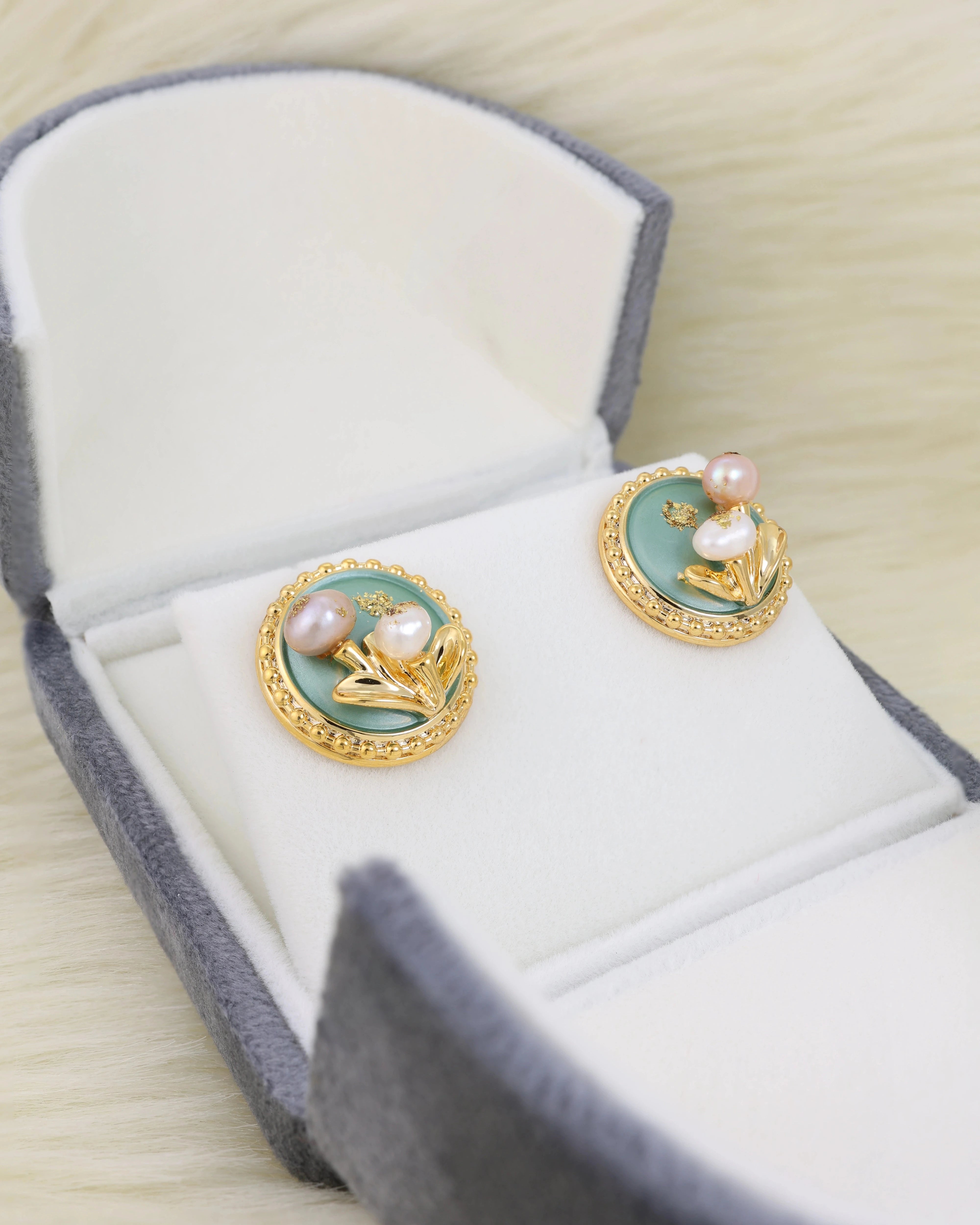 Pair of gold earrings with pearls in a jewelry box on a light fur surface