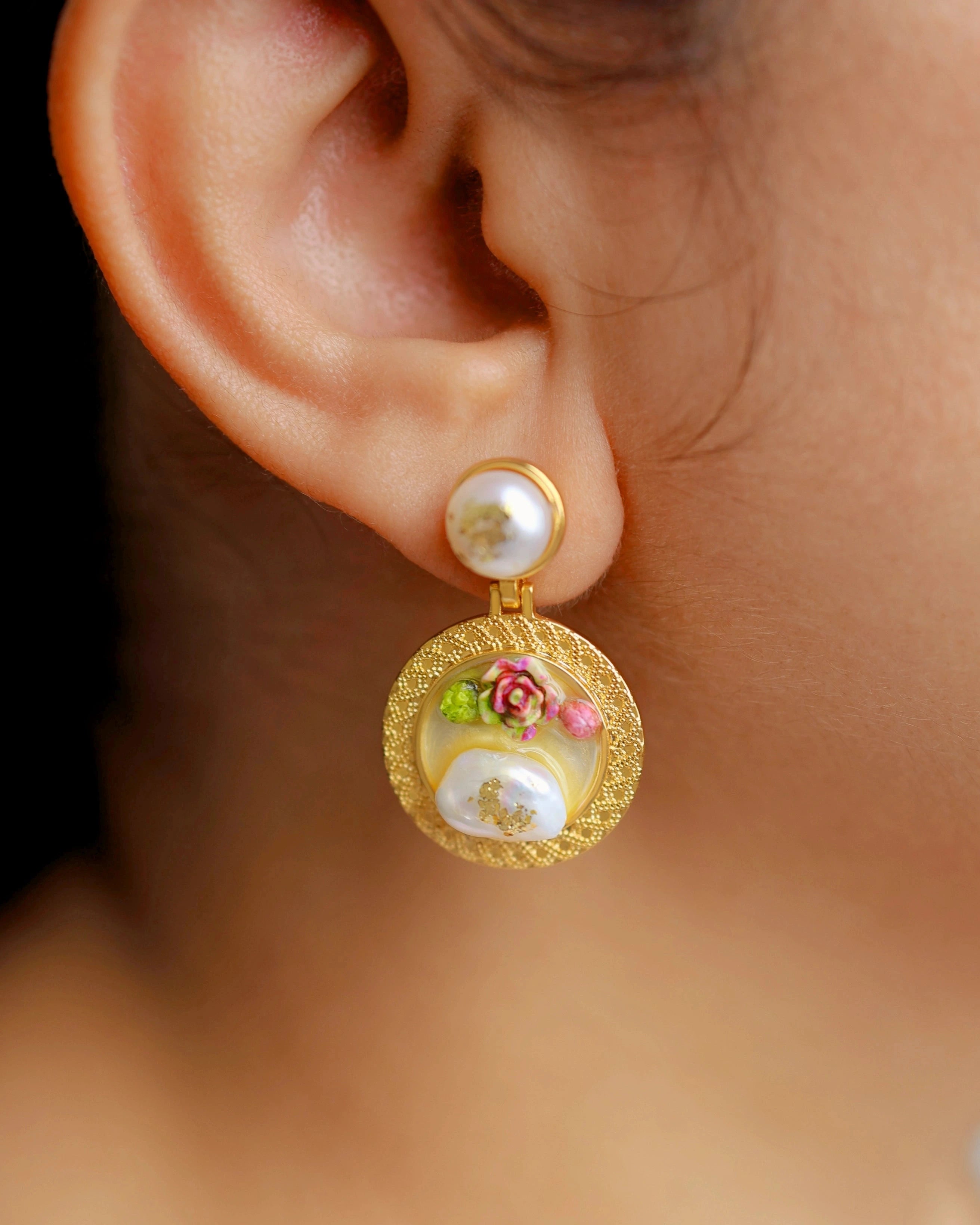 Gold earring with floral design worn by a person