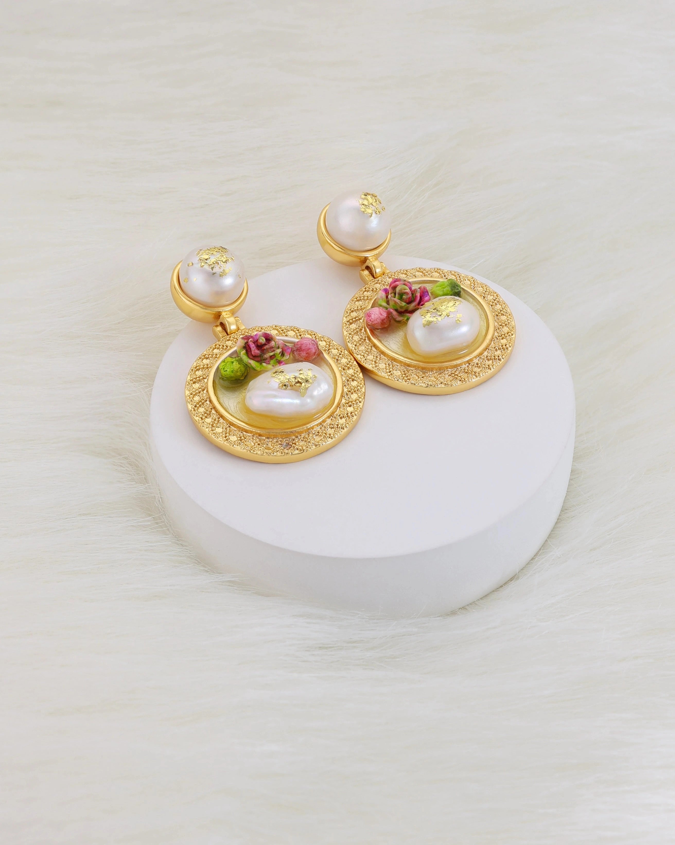 Gold earrings with pearls and floral elements on a white stand