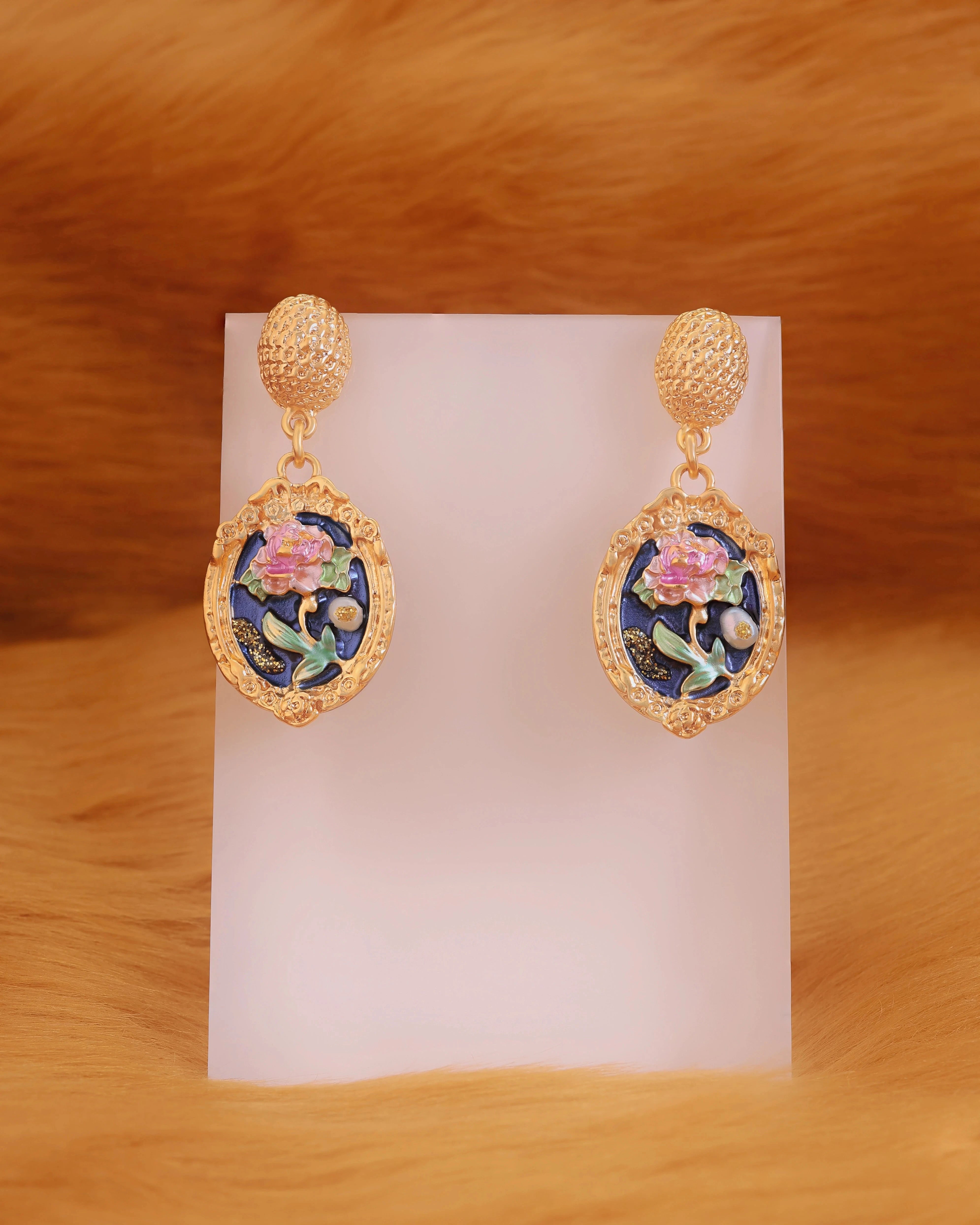Pair of gold earrings with floral design on a white card against a brown background