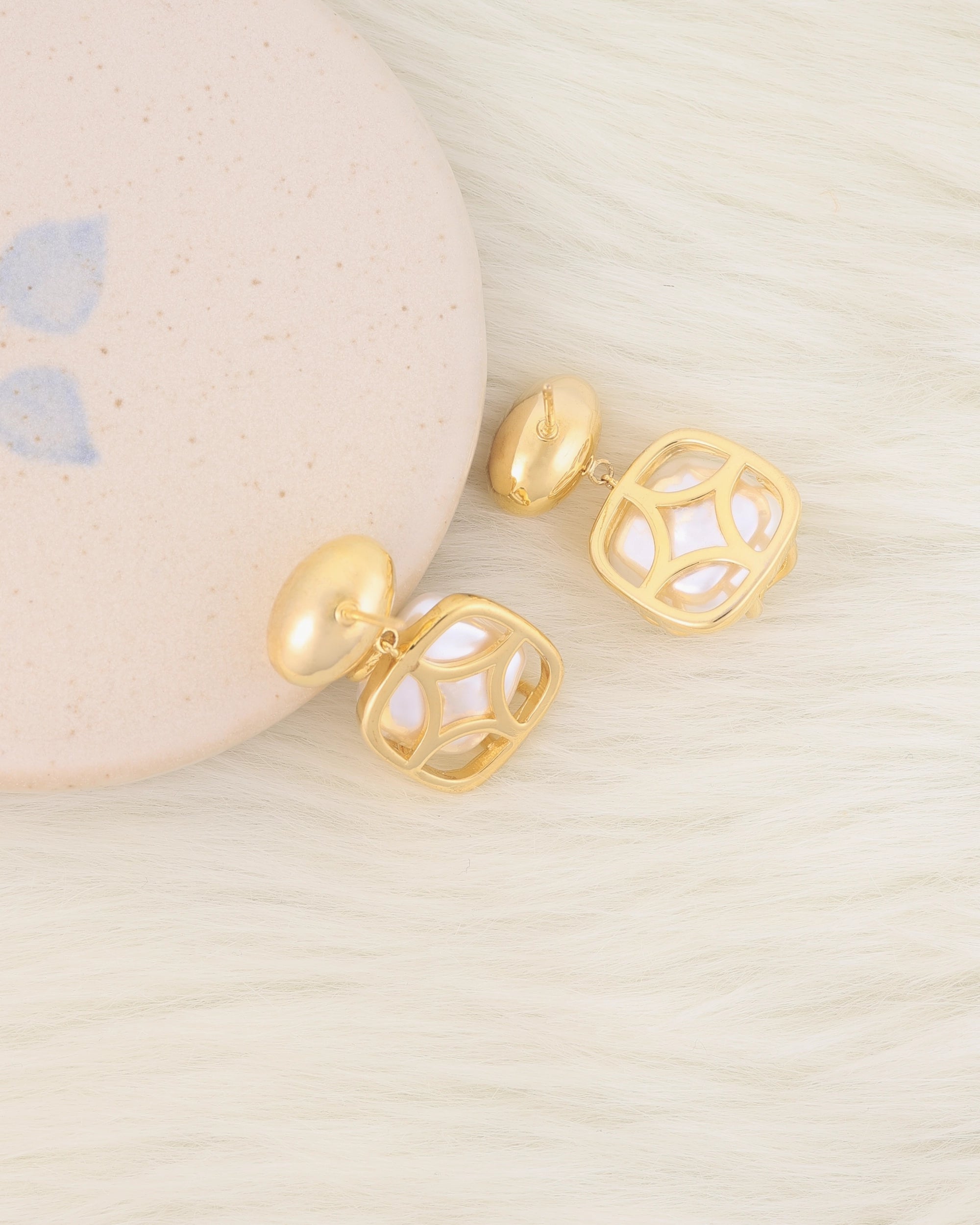 Gold earrings on a textured beige surface