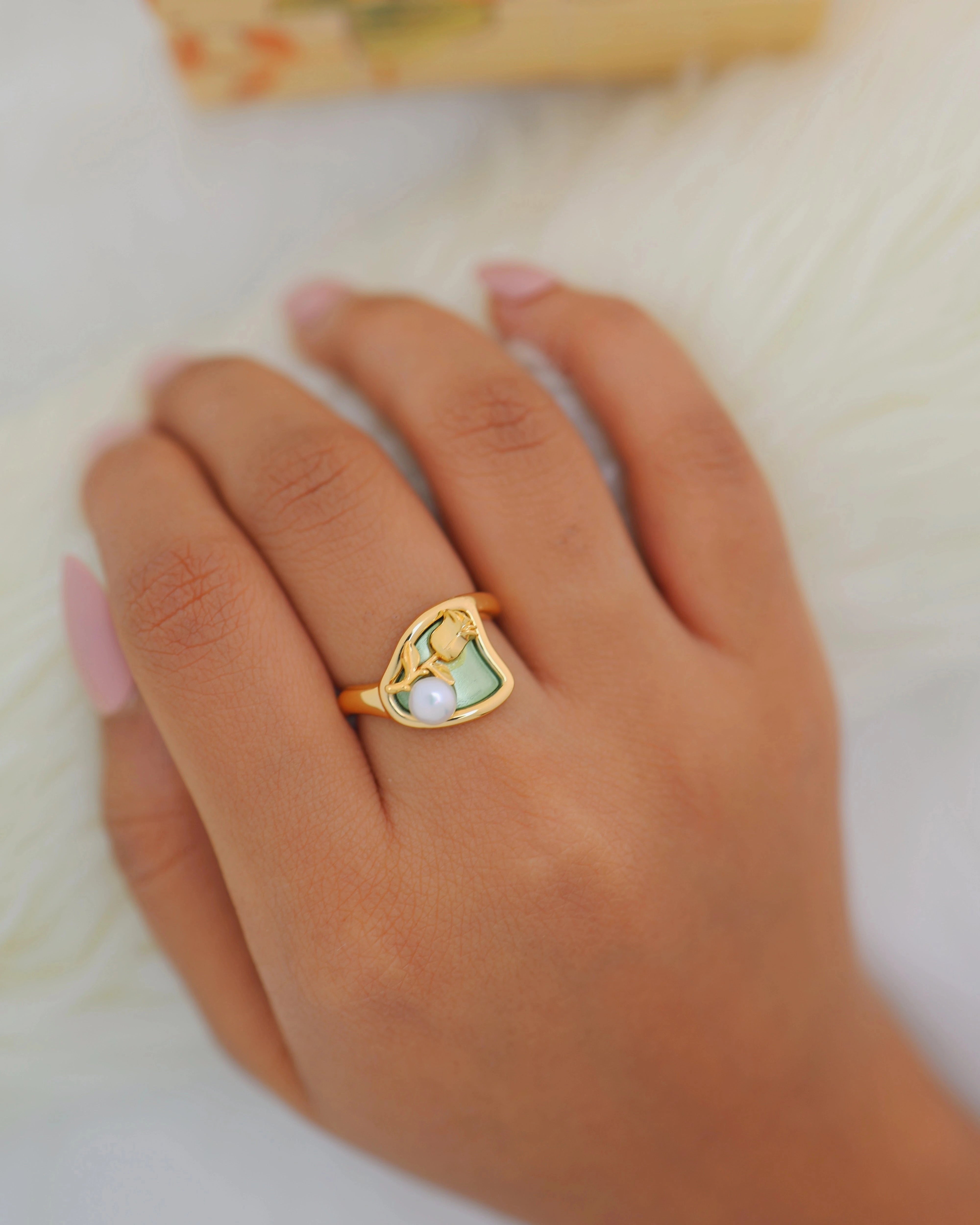 Gold ring with a heart-shaped pearl on a hand against a light background