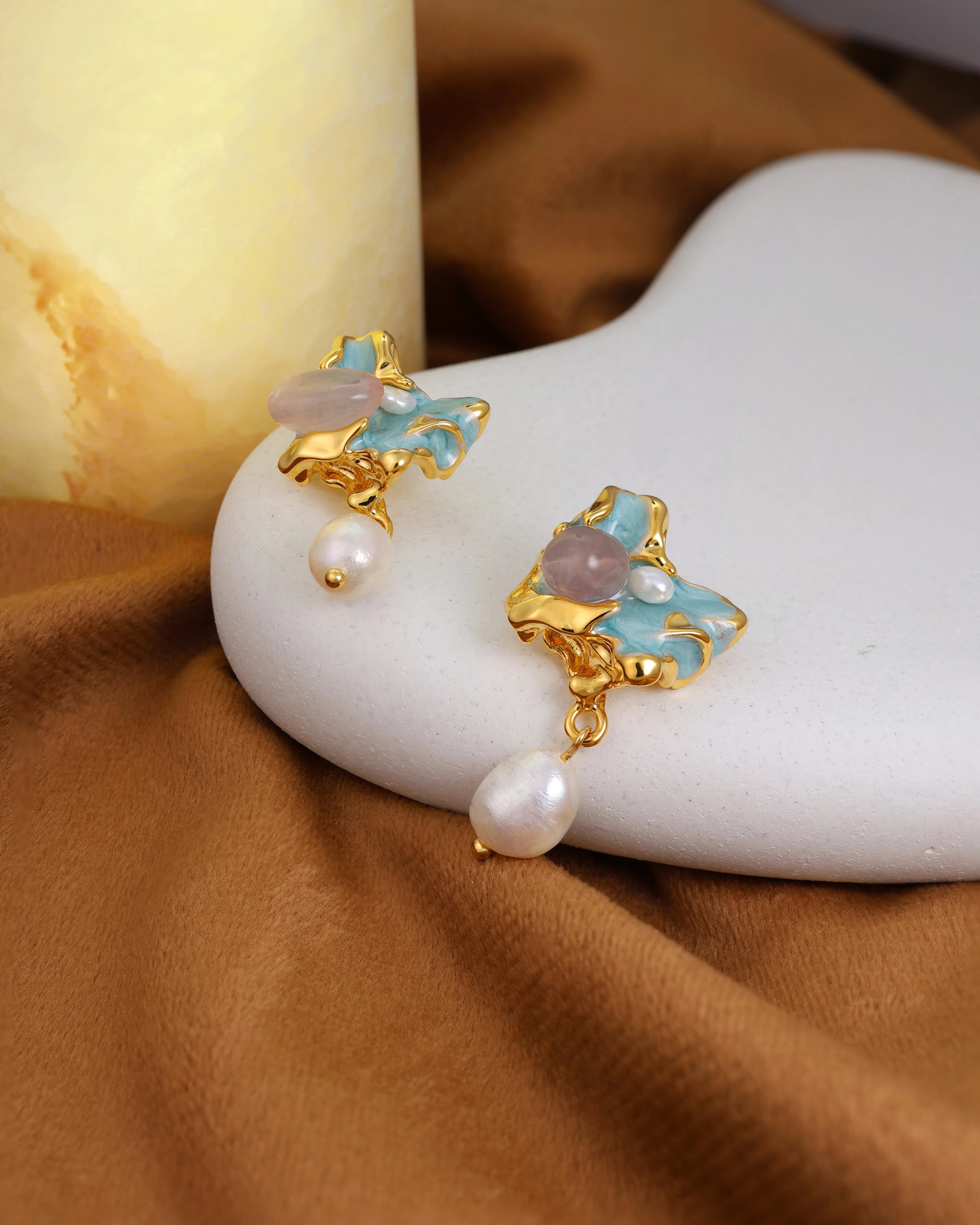 Gold and pearl earrings on a white stone with a brown fabric background