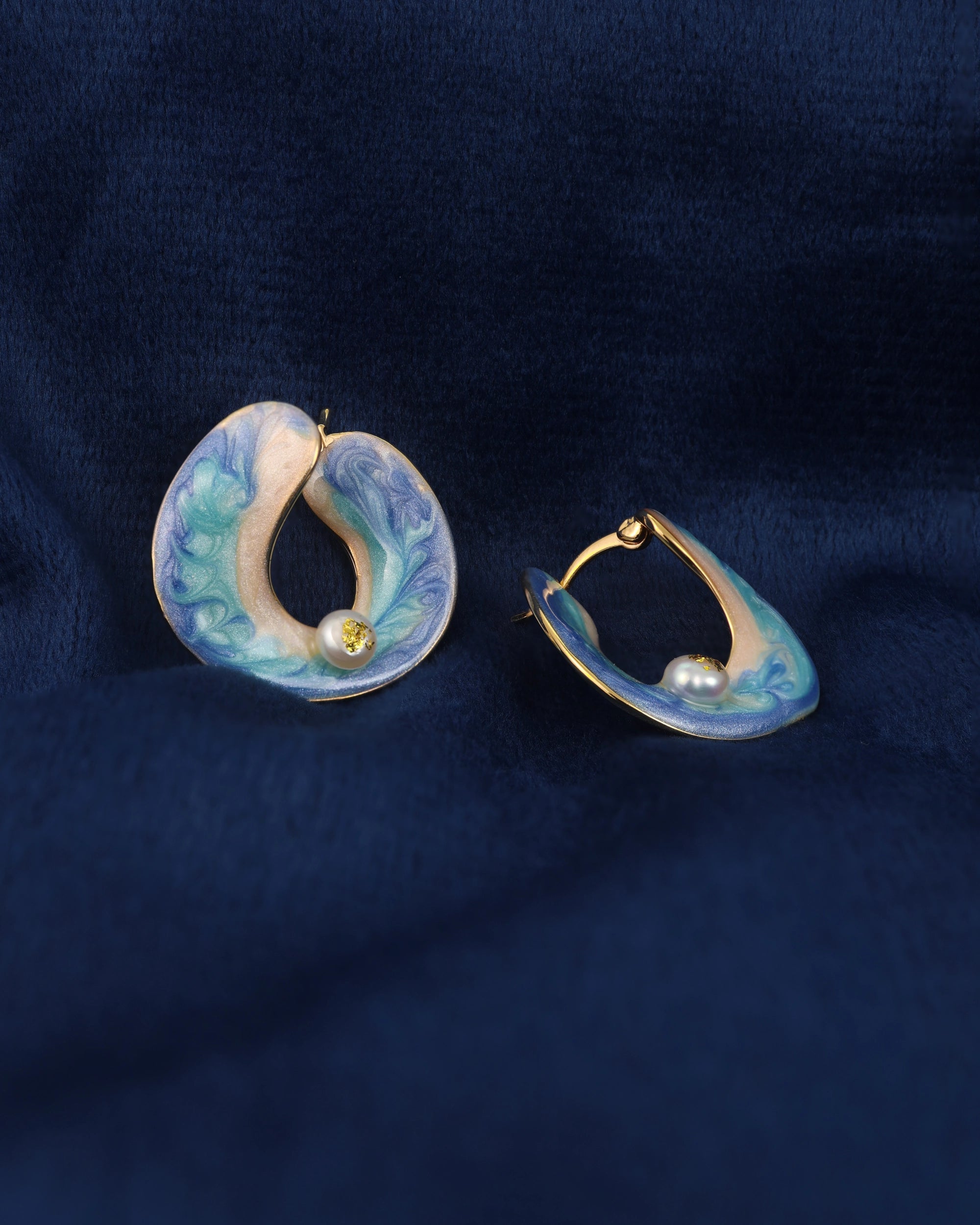 Pair of earrings with blue and gold design on a dark blue fabric background