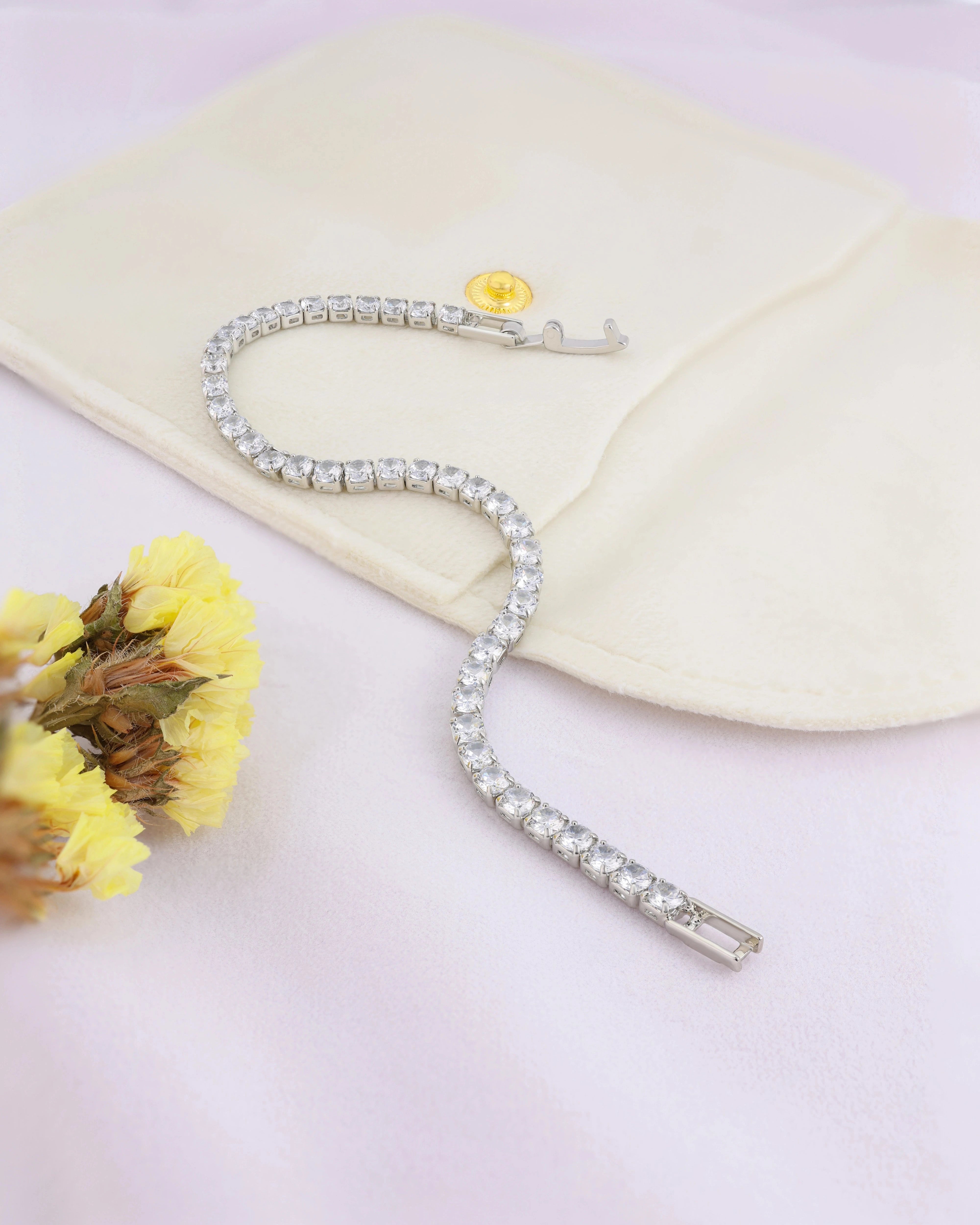 Silver bracelet with clear stones on a white surface with yellow flowers
